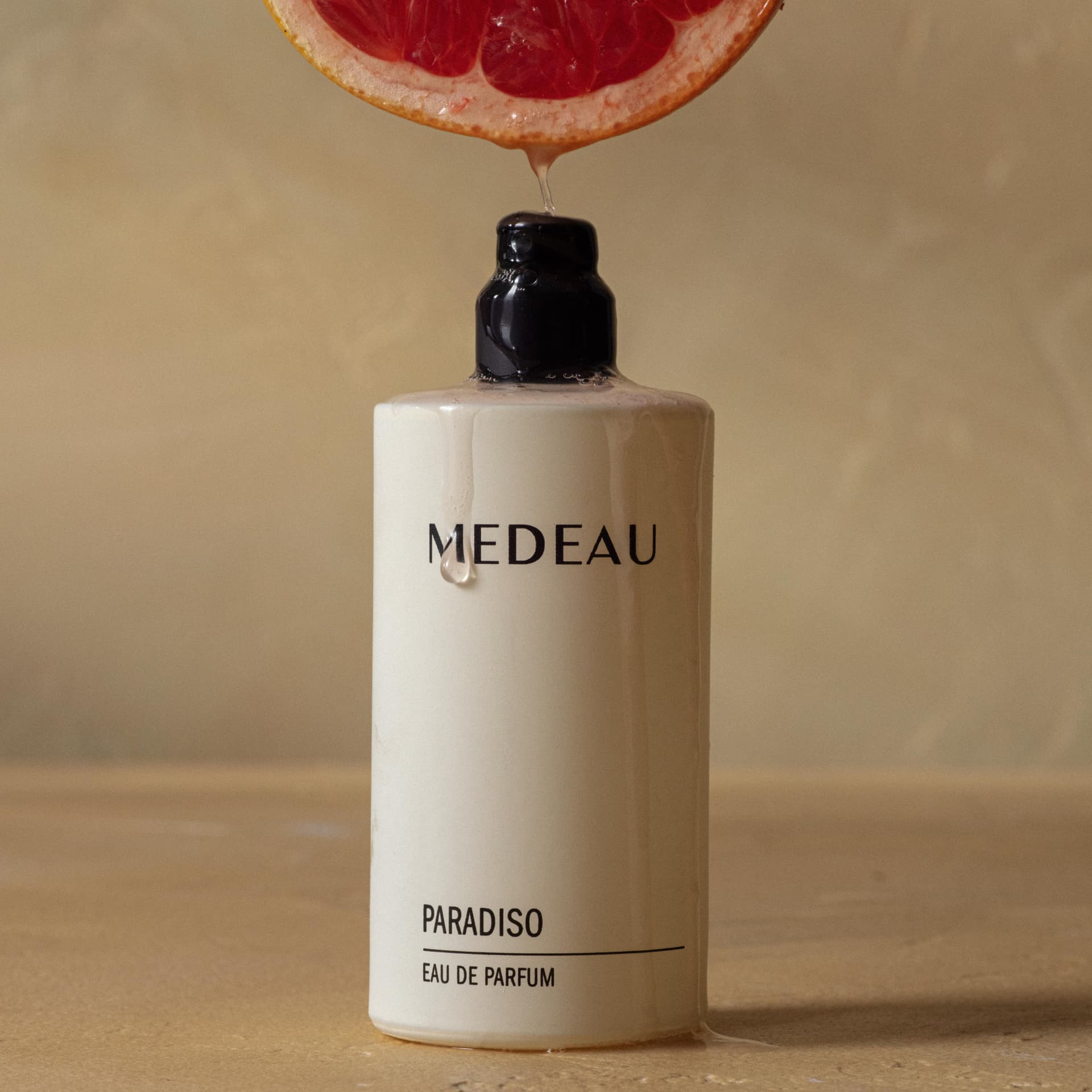 A bottle of Medeau Paradiso eau de parfum with grapefruit juice running over it
