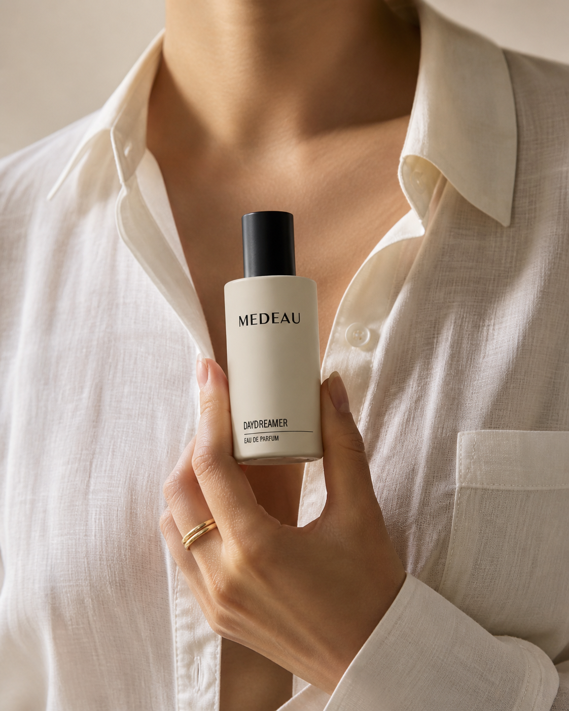 A woman in a white linen shirt holding a bottle of Medeau Daydreamer eau de parfum